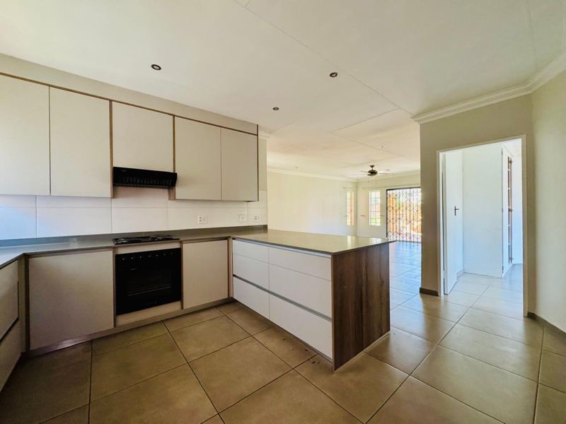 Modern open-plan kitchen featuring neutral cabinetry, built-in oven, hob, and extractor fan, flowing into a spacious living area with tiled floors throughout.