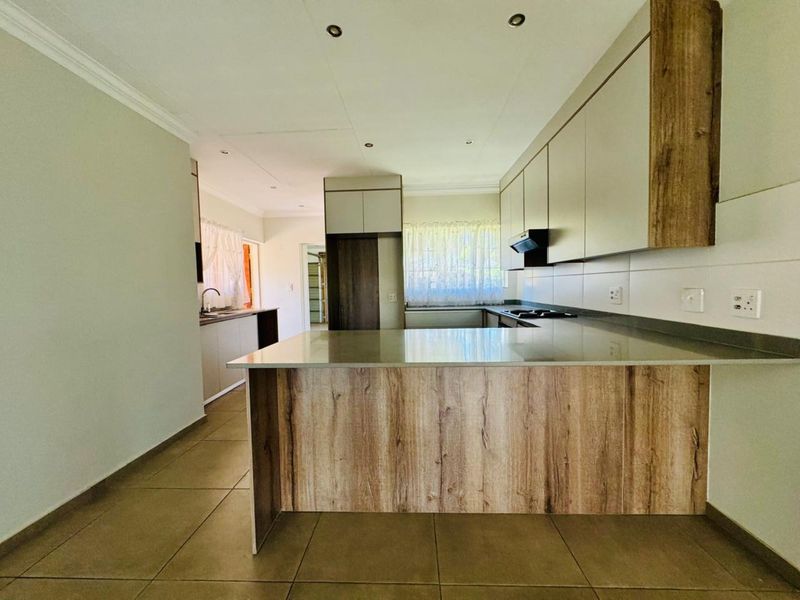Modern kitchen featuring wood-grain and neutral cabinetry, stone countertops, a central island, and integrated hob with extractor fan.
