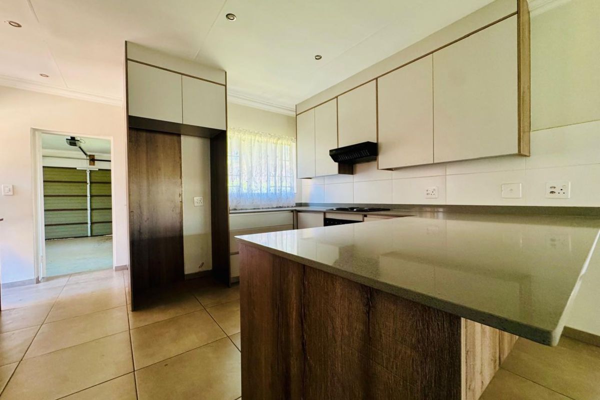 A modern kitchen featuring neutral-toned cabinetry, stone countertops, a built-in hob with extractor fan, and tiled flooring, leading directly into the garage area.