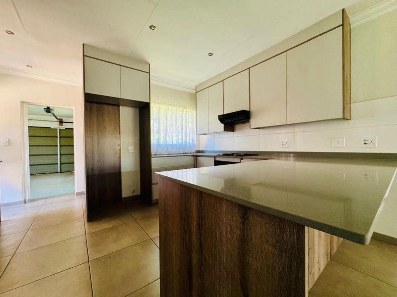 A modern kitchen featuring neutral-toned cabinetry, stone countertops, a built-in hob with extractor fan, and tiled flooring, leading directly into the garage area.