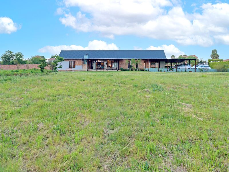 A wide-angle view of the rear elevation of a brick house featuring a metal roof, covered patio area, and an expansive surrounding garden.