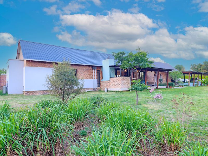 A view of the rear elevation featuring a brick facade, metal roofing, and a spacious covered patio overlooking a well-maintained garden.