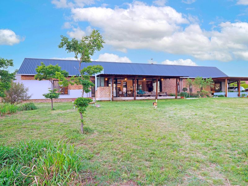 Rear view of a single-story home featuring exposed brickwork, a large covered patio area, and a spacious garden.
