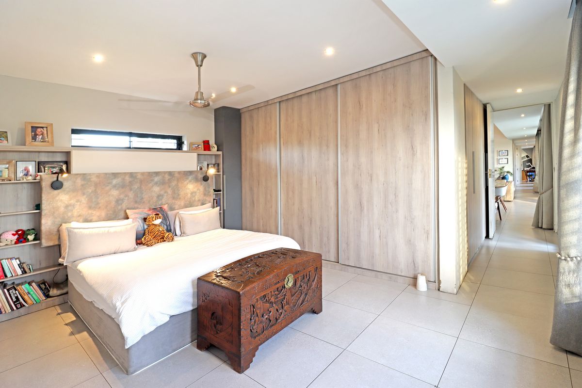 Spacious bedroom featuring modern tiled flooring, extensive built-in cupboards with wood-look finish, recessed lighting, and a ceiling fan.