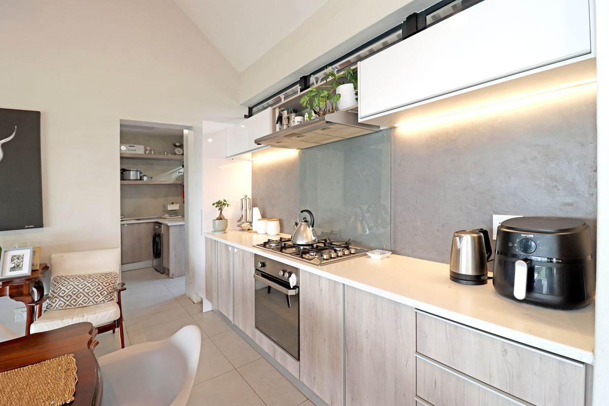 Modern kitchen featuring sleek wood-grain cabinetry, stone countertops, a gas hob with extractor, and integrated lighting, with an adjacent scullery area.