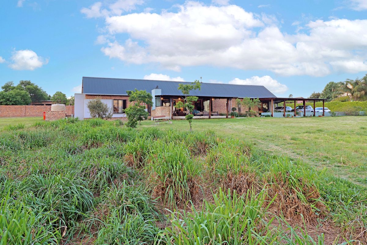 Rear view of a single-story brick house featuring a corrugated metal roof, a covered patio area, and a spacious garden.