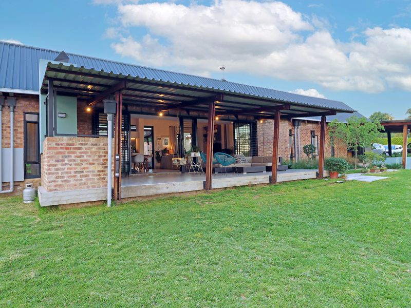A spacious rear exterior view featuring a covered patio with timber supports, exposed brickwork, and seamless access to the garden through sliding glass doors.