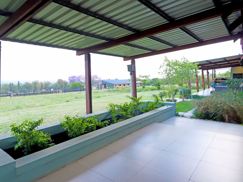 A spacious covered patio featuring tiled flooring, a built-in concrete planter, and steel structural supports, offering expansive views of the surrounding rural landscape.