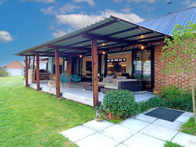 Spacious covered patio featuring a built-in braai, exposed brick walls, and timber support posts, seamlessly connecting to the interior living space.