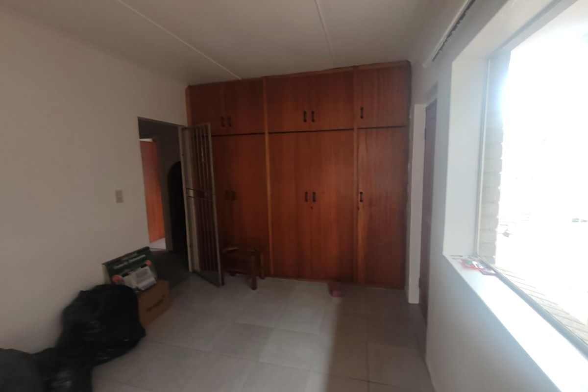 A bedroom featuring built-in wooden cupboards, tiled flooring, and a security gate, offering a functional space ready for personalization.