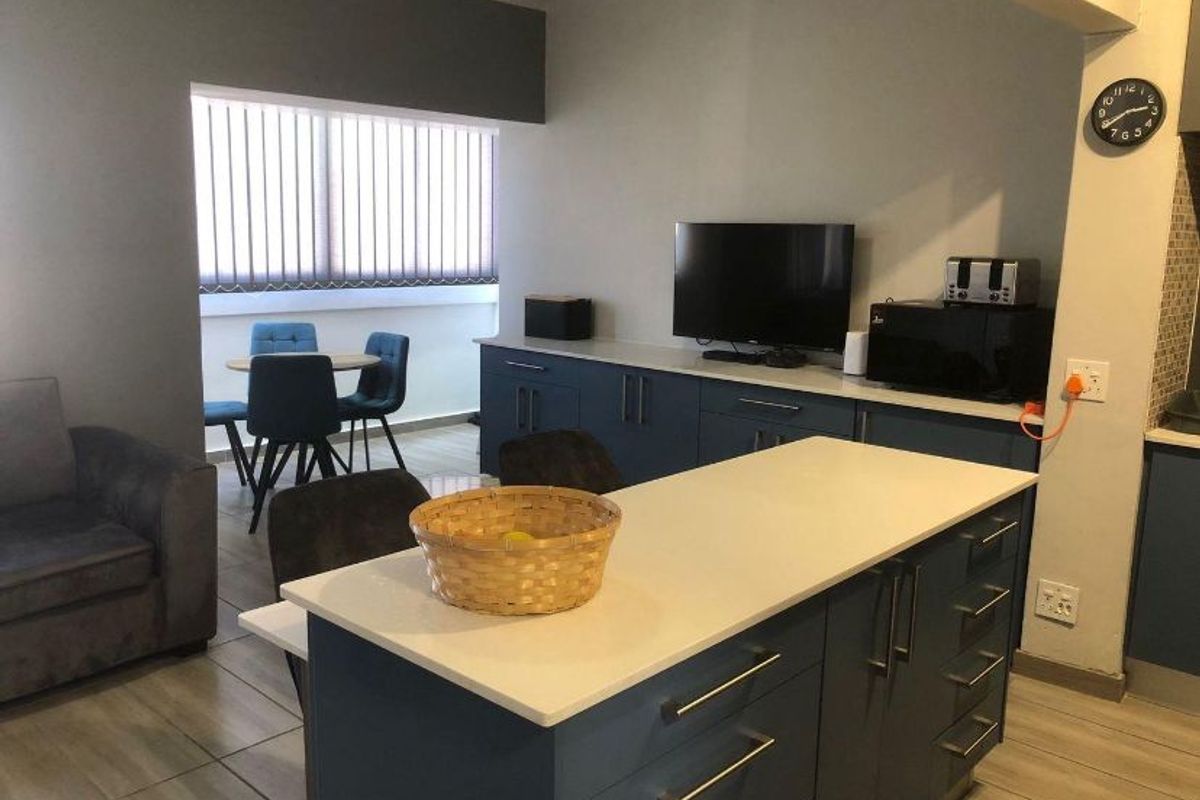 Open plan living and kitchen area featuring a central island with stone countertops, modern blue cabinetry, and tiled flooring throughout.