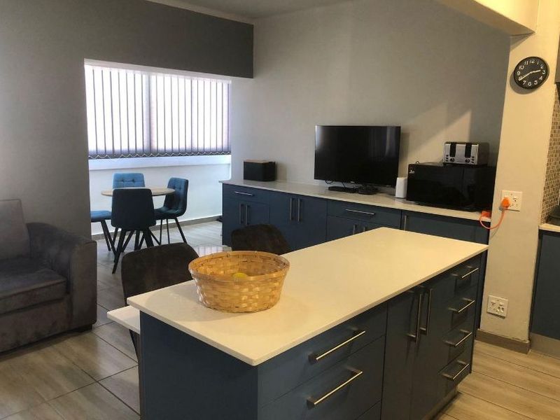 Open plan living and kitchen area featuring a central island with stone countertops, modern blue cabinetry, and tiled flooring throughout.
