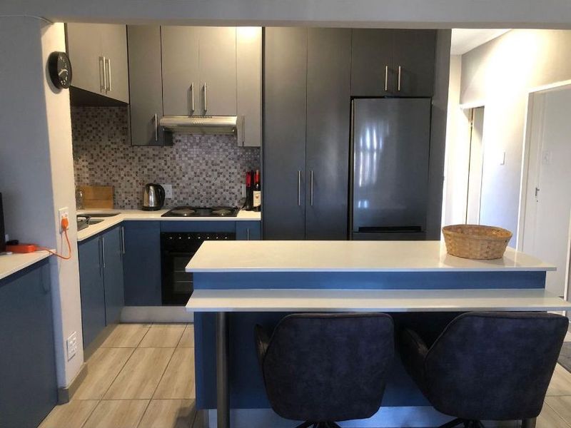 Modern kitchen featuring dark blue cabinetry, stone countertops, a breakfast bar, and a mosaic tile backsplash with integrated appliances.