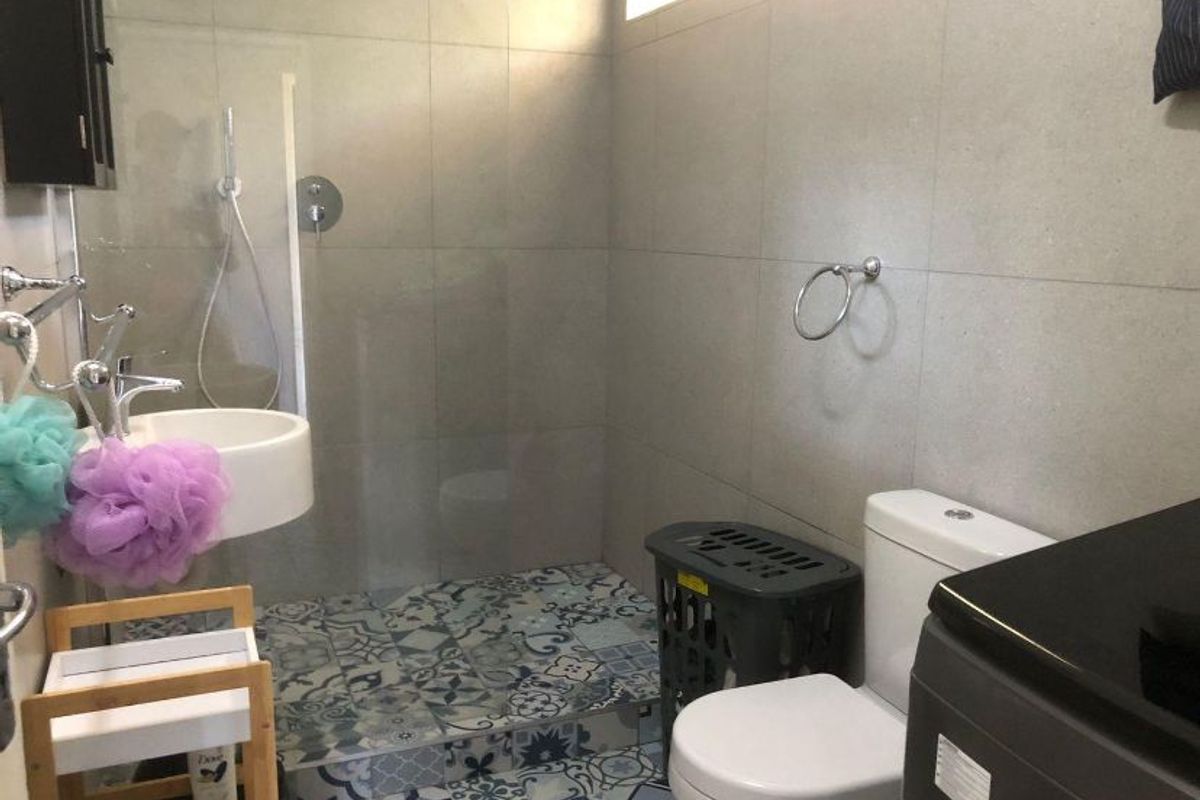 A modern bathroom featuring a walk-in shower with glass screen, patterned floor tiles, wall-mounted basin, and a standard toilet.
