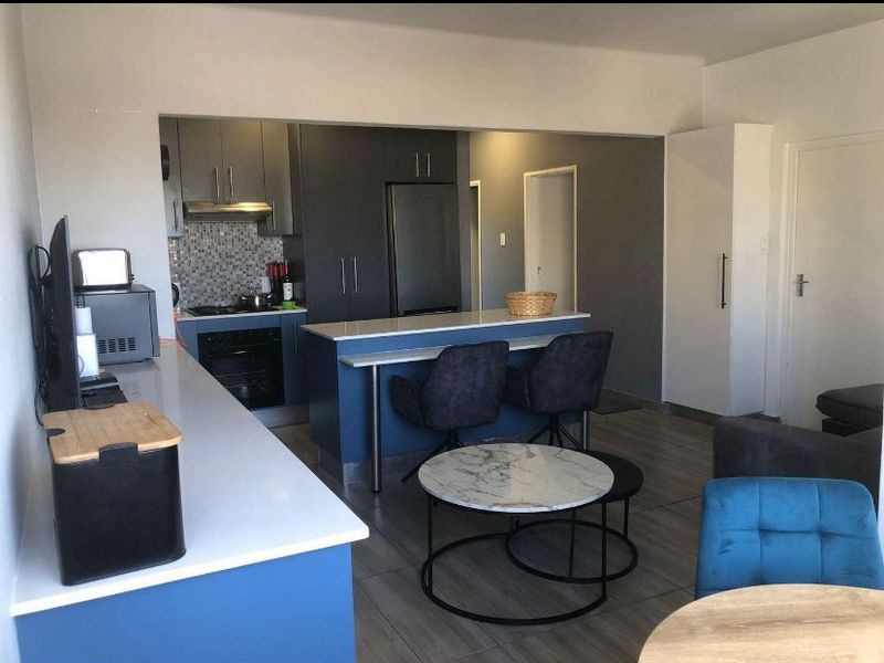 Modern open-plan kitchen featuring blue cabinetry, stone countertops, a breakfast island, and integrated appliances, seamlessly flowing into the living area.