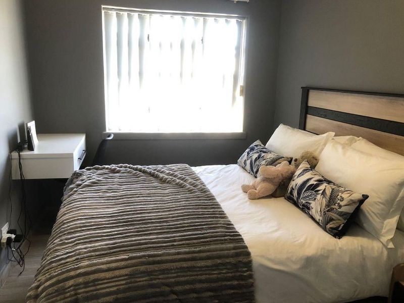 A well-maintained bedroom featuring neutral grey walls, laminate flooring, and vertical window blinds, providing a comfortable and functional living space.