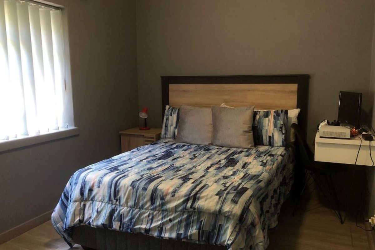 A functional bedroom featuring laminate flooring and vertical window blinds, providing a neutral base for personal styling.