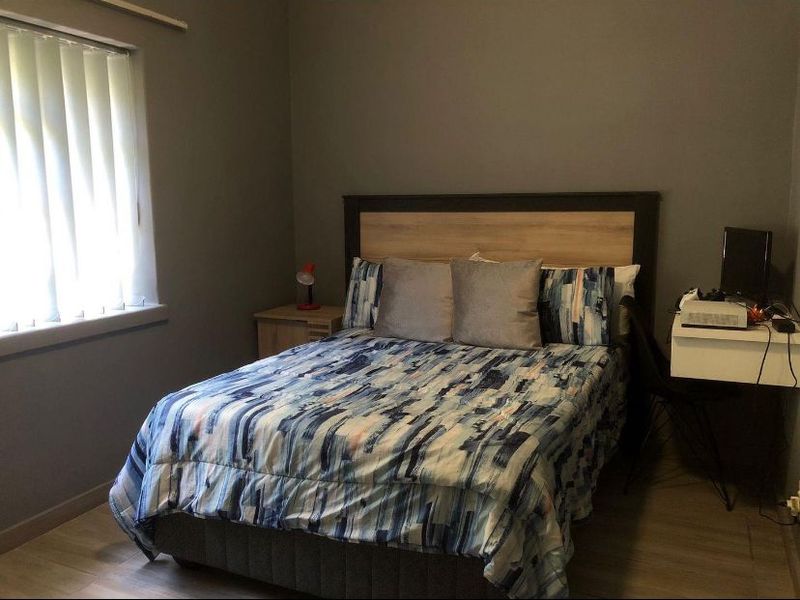 A functional bedroom featuring laminate flooring and vertical window blinds, providing a neutral base for personal styling.