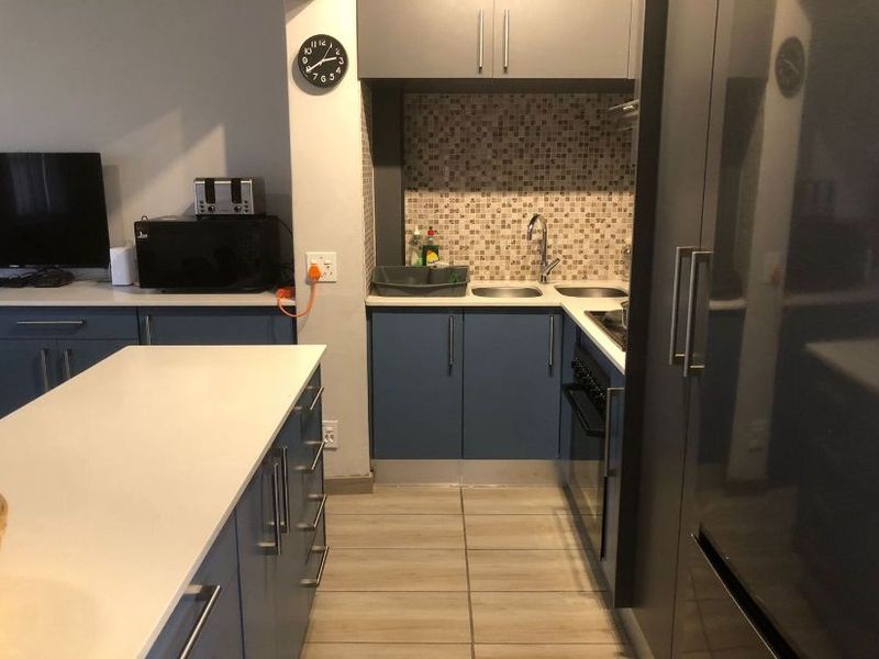 Modern kitchen featuring blue cabinetry, stone countertops, a mosaic tile backsplash, and a functional kitchen island with integrated appliances.