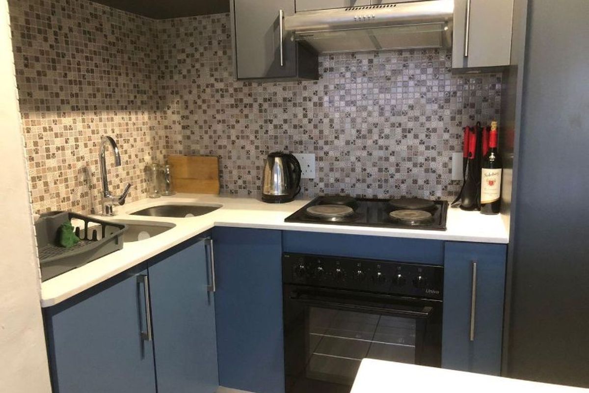 Compact kitchen featuring blue and grey cabinetry, mosaic tile backsplash, stone countertops, and integrated stainless steel appliances including an oven and extractor fan.