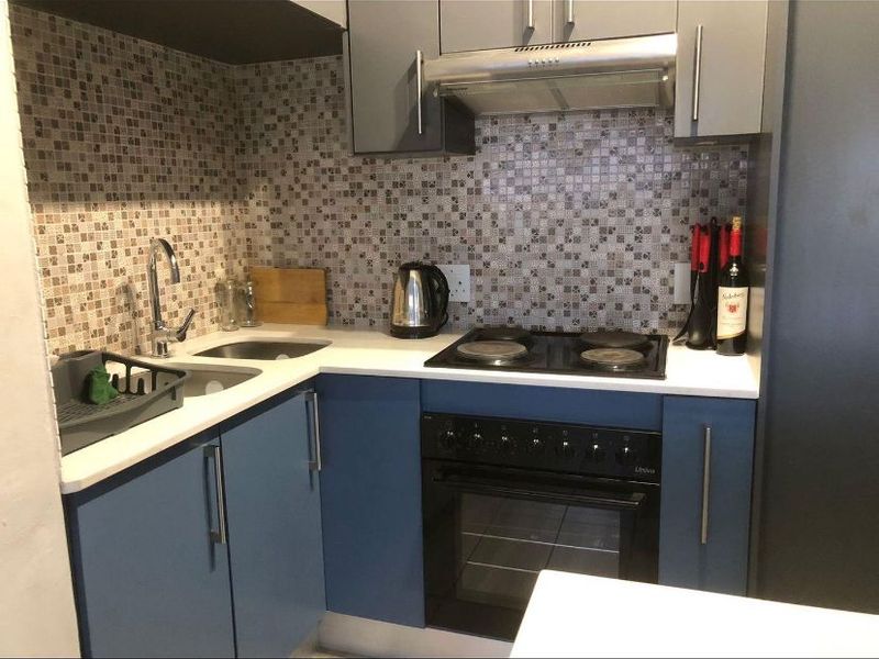 Compact kitchen featuring blue and grey cabinetry, mosaic tile backsplash, stone countertops, and integrated stainless steel appliances including an oven and extractor fan.