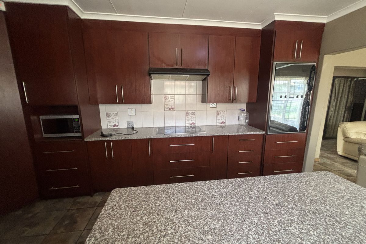 A functional kitchen featuring dark wood cabinetry, granite countertops, a built-in oven, and an electric hob with a tiled backsplash.