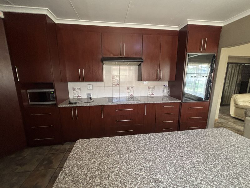 A functional kitchen featuring dark wood cabinetry, granite countertops, a built-in oven, and an electric hob with a tiled backsplash.