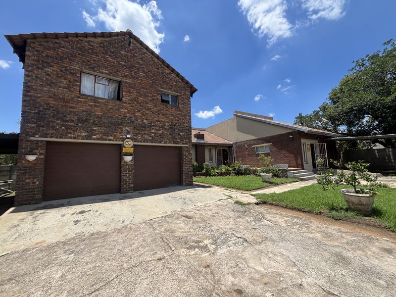 Front view of a double-story brick house featuring a double garage, concrete driveway, and established garden area.