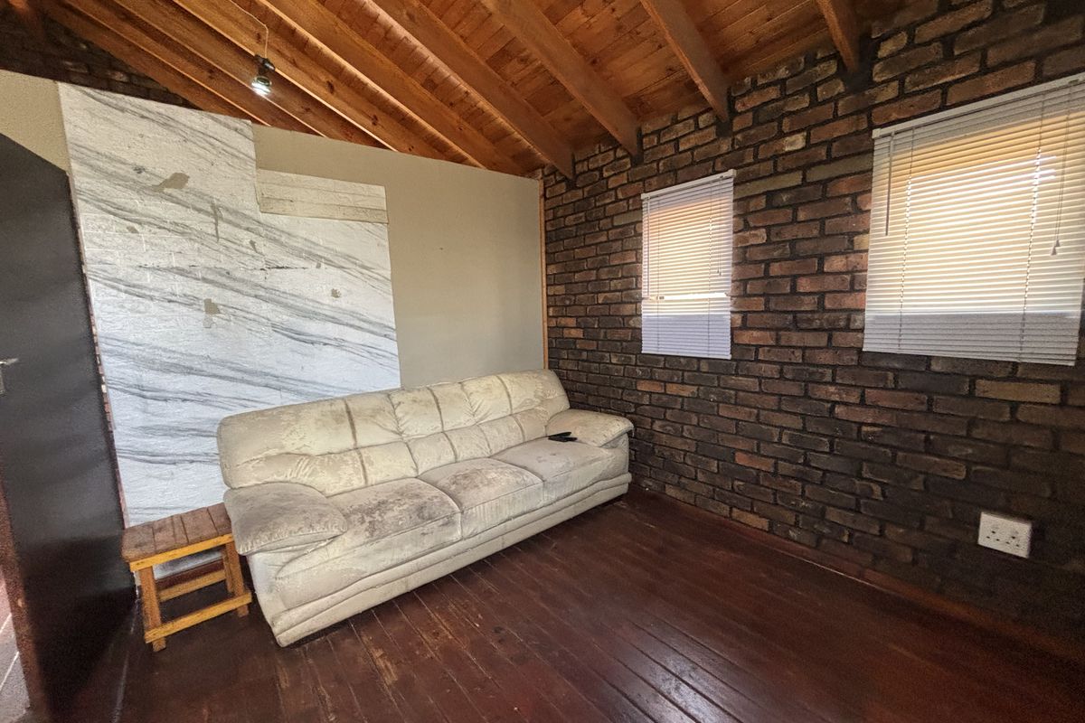 Living room featuring exposed brick walls, high timber beam ceilings, and hardwood flooring, offering a rustic aesthetic with potential for modern updates.