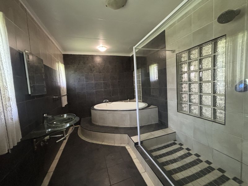 Spacious bathroom featuring a raised built-in bathtub, a separate glass-enclosed shower, and a modern glass vessel sink with dark tiled finishes.
