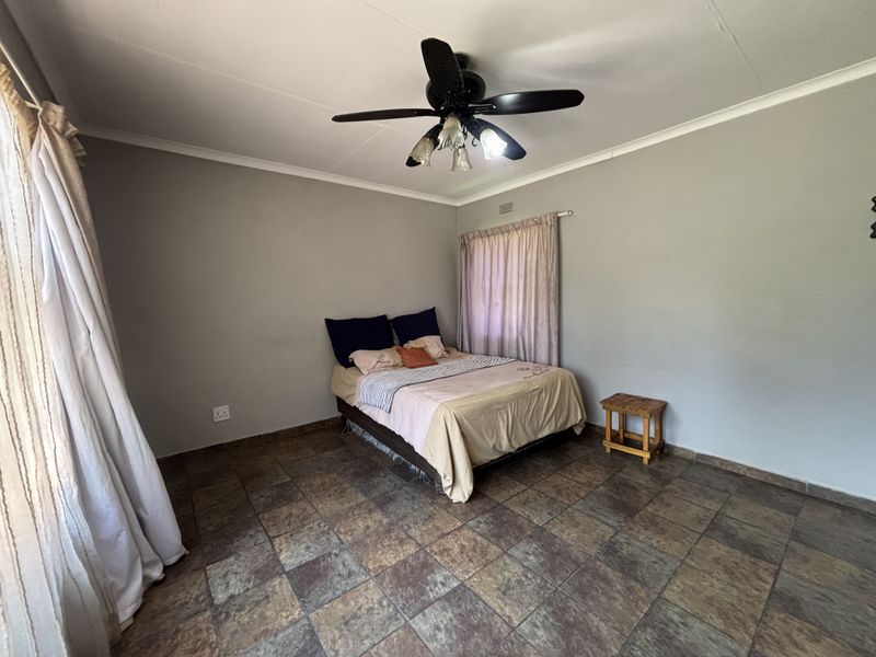 A spacious bedroom featuring tiled flooring, coved cornicing, and a central ceiling fan, providing a neutral foundation for interior design updates.