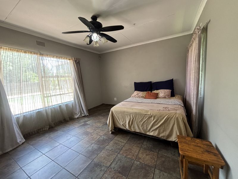 Spacious bedroom featuring tiled flooring, a ceiling fan, and large windows allowing for natural light.
