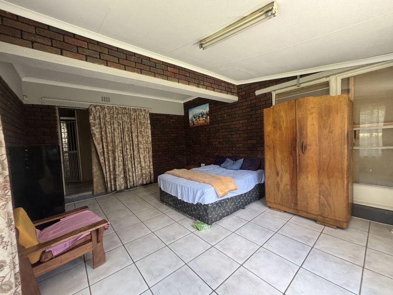 Spacious bedroom featuring exposed brick walls and ceramic tiled flooring, offering a rustic aesthetic with potential for modern updates.