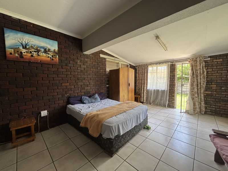 Spacious bedroom featuring exposed brick walls, ceramic tiled flooring, and direct access to the garden through a security gate.