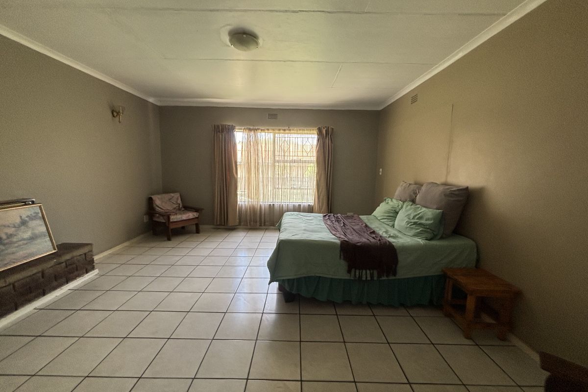 Spacious bedroom featuring tiled flooring, a built-in brick fireplace, and large window with natural light.
