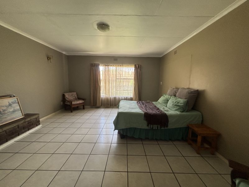 Spacious bedroom featuring tiled flooring, a built-in brick fireplace, and large window with natural light.