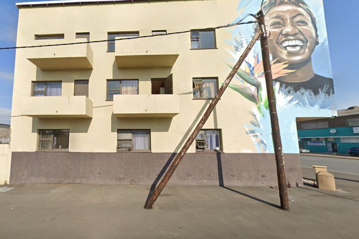 Exterior view of a multi-story apartment building featuring a prominent large-scale wall mural, multiple balconies, and sliding window units.