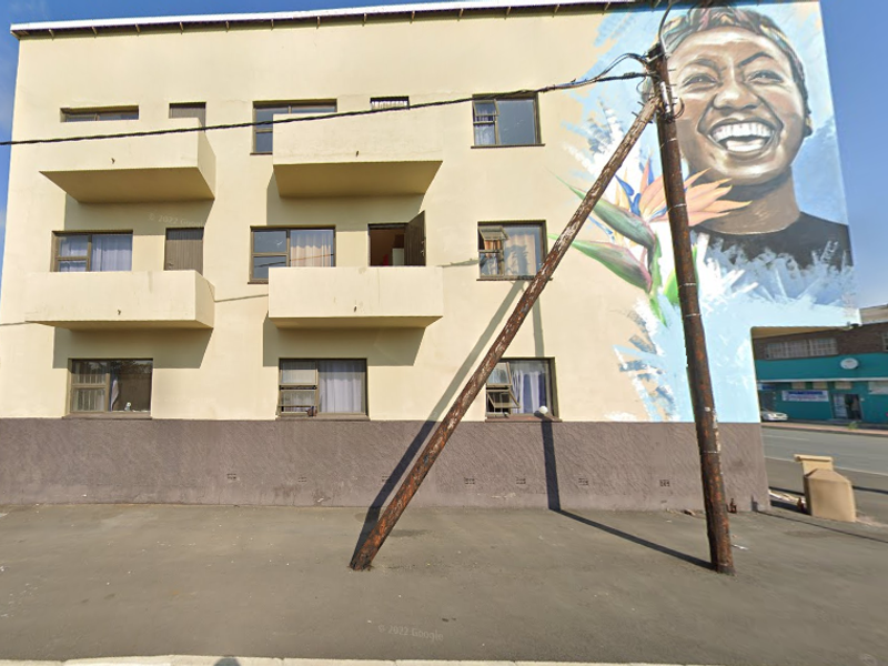 Exterior view of a multi-story apartment building featuring a prominent large-scale wall mural, multiple balconies, and sliding window units.