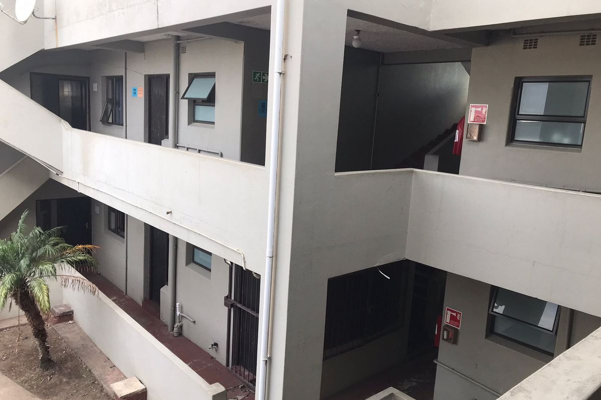 Exterior view of an apartment building showing concrete walkways, stairwells, and security features with visible signs of weathering.