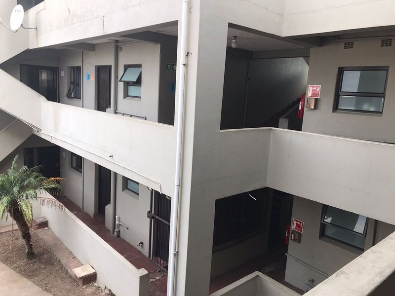 Exterior view of an apartment building showing concrete walkways, stairwells, and security features with visible signs of weathering.