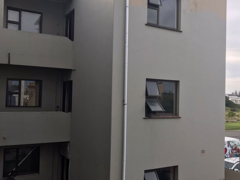 Exterior view of an apartment building showing the rear facade, external stairwell access, and communal concrete laundry wash troughs.