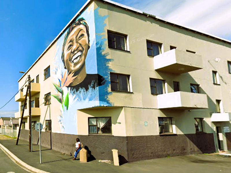 Exterior view of a multi-story apartment building featuring a prominent mural on the corner facade and multiple private balconies.