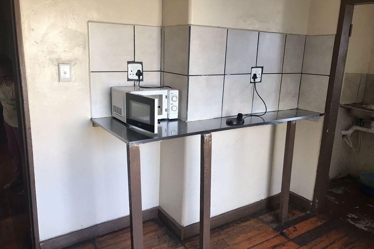A basic kitchen prep area featuring a stainless steel countertop, tiled backsplash, and wooden flooring, currently in need of cosmetic updates and refurbishment.