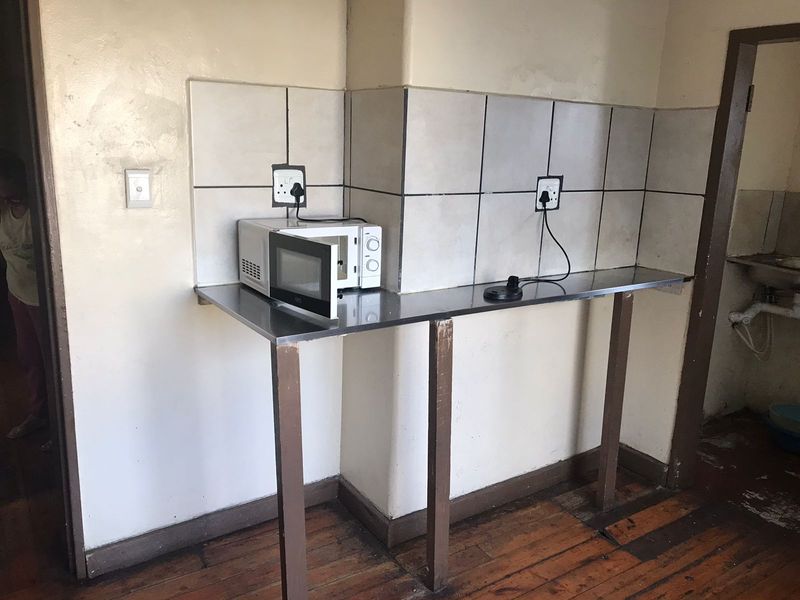 A basic kitchen prep area featuring a stainless steel countertop, tiled backsplash, and wooden flooring, currently in need of cosmetic updates and refurbishment.