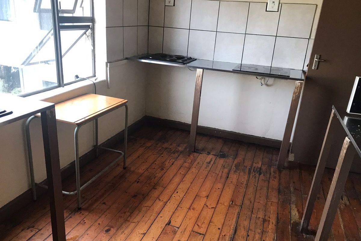 A basic kitchen area featuring a built-in hob, tiled backsplash, and original timber flooring, requiring significant renovation and cosmetic updates.