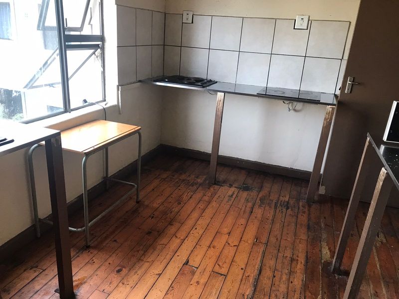 A basic kitchen area featuring a built-in hob, tiled backsplash, and original timber flooring, requiring significant renovation and cosmetic updates.