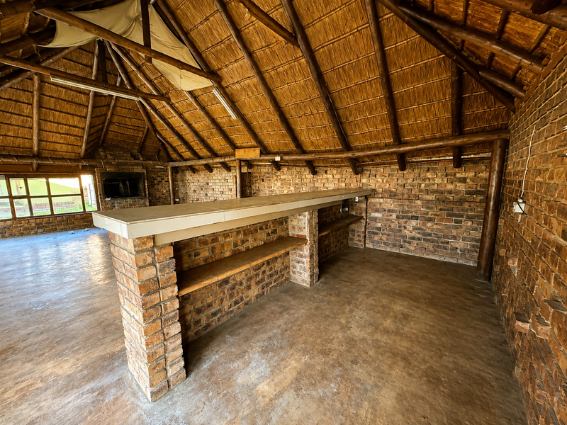Spacious entertainment area featuring a rustic thatched roof, exposed timber beams, brick walls, and a built-in brick bar counter with a fireplace.