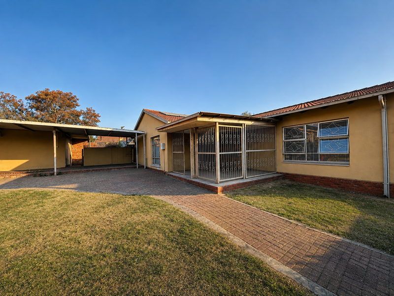 Rear view of the property featuring a paved courtyard, covered carport, and secure entrance with security gates and bars.