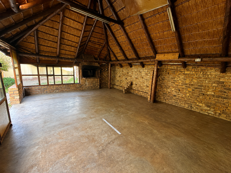 Spacious covered patio featuring a traditional thatched roof, exposed timber beams, brick walls, and a built-in fireplace, offering a rustic outdoor entertainment space.