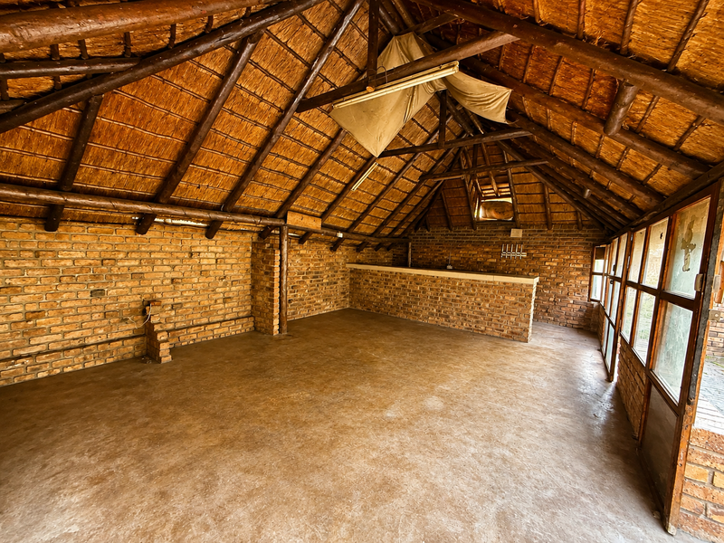 Spacious entertainment area featuring a rustic thatched roof, exposed timber trusses, brick walls, and a built-in brick bar counter.